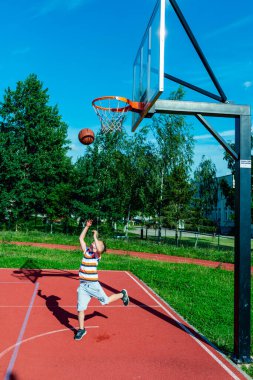Telsiai, Litvanya 08: 12 2020 Çekici Kafkasyalı küçük basketbolcu açık havada kırmızı kortta antrenman yapıyor.