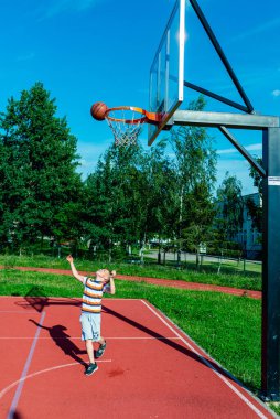 Telsiai, Litvanya 08: 12 2020 Çekici Kafkasyalı küçük basketbolcu açık havada kırmızı kortta antrenman yapıyor.