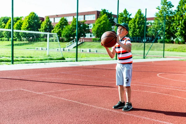 Telsiai, Litvanya 08: 12 2020 Çekici Kafkasyalı küçük basketbolcu açık havada kırmızı kortta antrenman yapıyor.