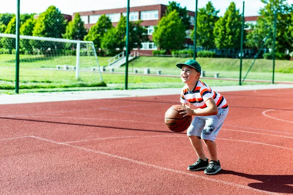 Telsiai, Litvanya 08: 12 2020 Çekici Kafkasyalı küçük basketbolcu açık havada kırmızı kortta antrenman yapıyor.