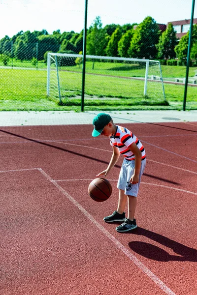 Telsiai, Litvanya 08: 12 2020 Çekici Kafkasyalı küçük basketbolcu açık havada kırmızı kortta antrenman yapıyor.