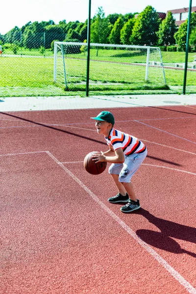 Telsiai, Litvanya 08: 12 2020 Çekici Kafkasyalı küçük basketbolcu açık havada kırmızı kortta antrenman yapıyor.