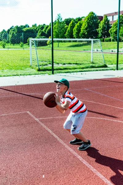 Telsiai, Litvanya 08: 12 2020 Çekici Kafkasyalı küçük basketbolcu açık havada kırmızı kortta antrenman yapıyor.