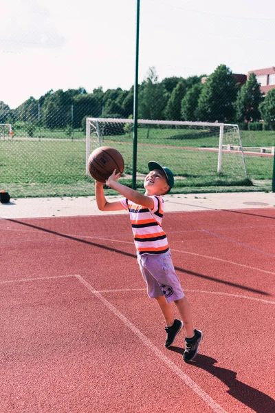 Telsiai, Litvanya 08: 12 2020 Çekici Kafkasyalı küçük basketbolcu açık havada kırmızı kortta antrenman yapıyor.