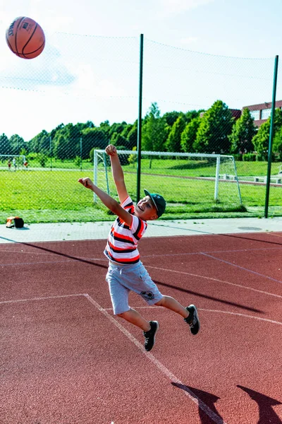Telsiai, Litvanya 08: 12 2020 Çekici Kafkasyalı küçük basketbolcu açık havada kırmızı kortta antrenman yapıyor.