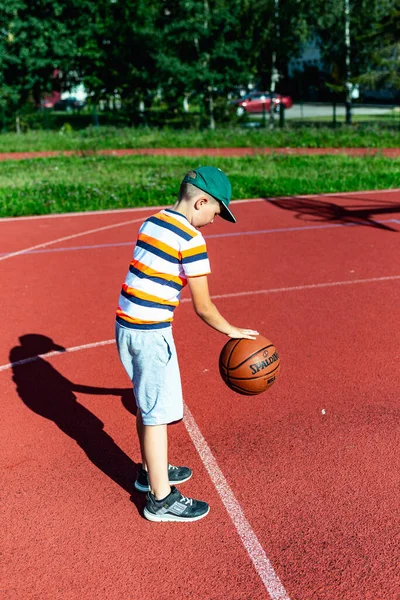 Telsiai, Litvanya 08: 12 2020 Çekici Kafkasyalı küçük basketbolcu açık havada kırmızı kortta antrenman yapıyor.