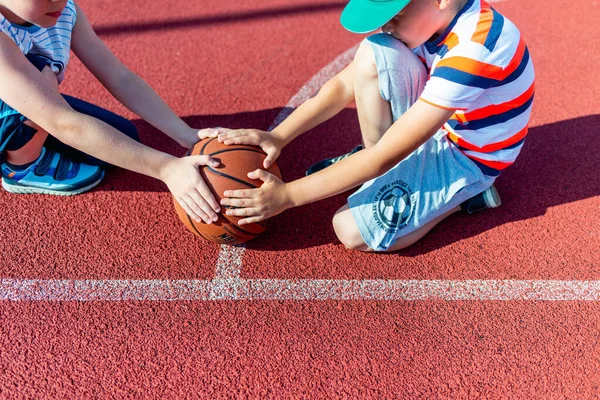 Telsiai Litvanis 08: 12 2020 Açık hava kırmızı kortunda oturan iki küçük basketbolcu. Kopya alanı olan basketbol sahası arkaplanı.