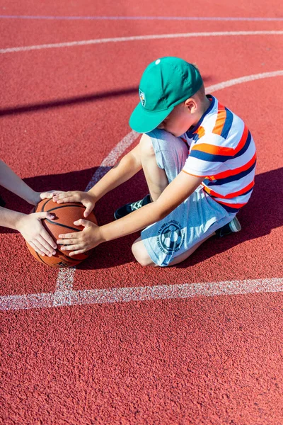 Telsiai Litvanis 08: 12 2020 Açık hava kırmızı kortunda oturan iki küçük basketbolcu. Kopya alanı olan basketbol sahası arkaplanı.