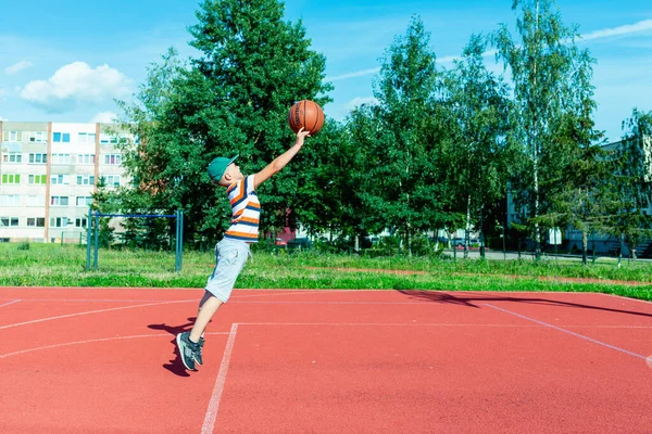 Telsiai, Litvanya 08: 12 2020 Çekici Kafkasyalı küçük basketbolcu açık havada kırmızı kortta antrenman yapıyor.
