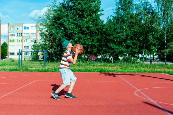 Telsiai, Litvanya 08: 12 2020 Çekici Kafkasyalı küçük basketbolcu açık havada kırmızı kortta antrenman yapıyor.