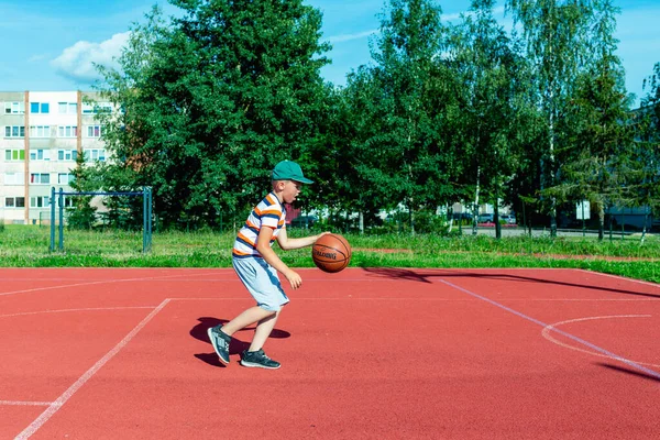 Telsiai, Litvanya 08: 12 2020 Çekici Kafkasyalı küçük basketbolcu açık havada kırmızı kortta antrenman yapıyor.