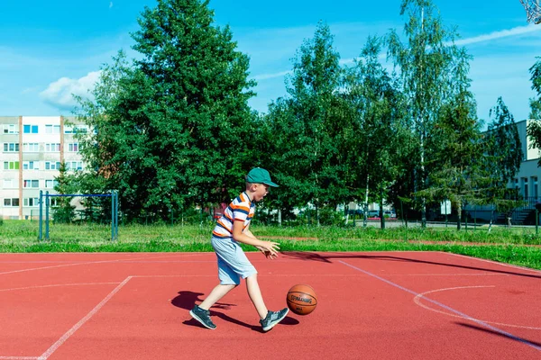 Telsiai, Litvanya 08: 12 2020 Çekici Kafkasyalı küçük basketbolcu açık havada kırmızı kortta antrenman yapıyor.