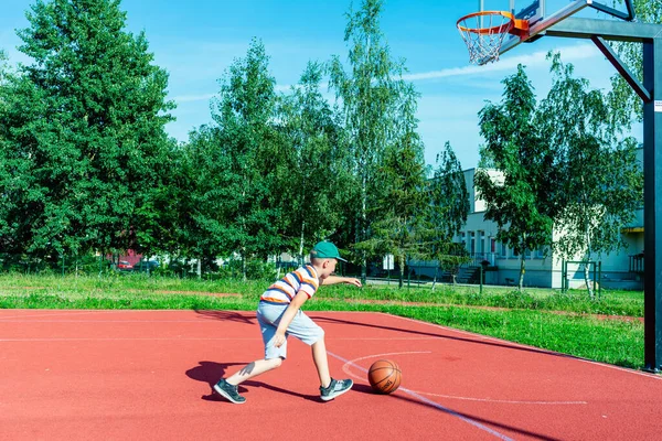 Telsiai, Litvanya 08: 12 2020 Çekici Kafkasyalı küçük basketbolcu açık havada kırmızı kortta antrenman yapıyor.