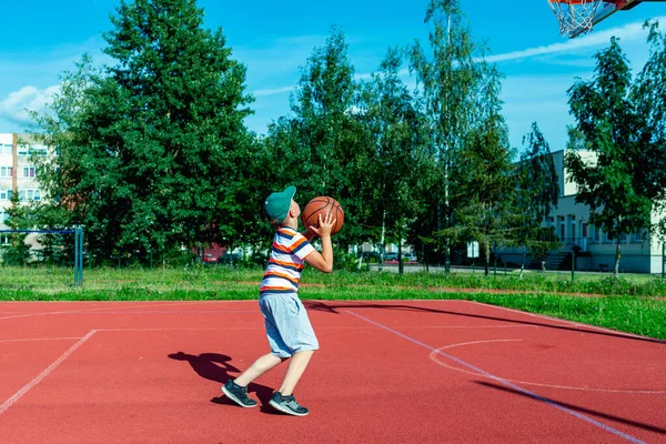 Telsiai, Litvanya 08: 12 2020 Çekici Kafkasyalı küçük basketbolcu açık havada kırmızı kortta antrenman yapıyor.