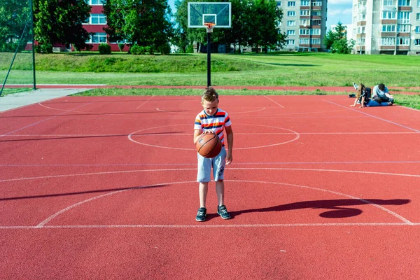 Telsiai, Litvanya 08: 12 2020 Çekici Kafkasyalı küçük basketbolcu açık havada kırmızı kortta antrenman yapıyor.