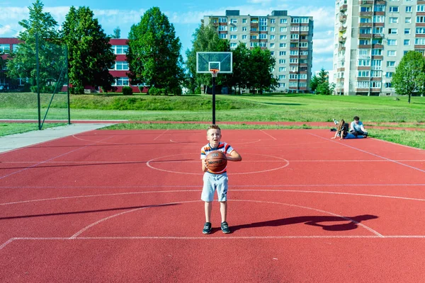 Telsiai, Litvanya 08: 12 2020 Çekici Kafkasyalı küçük basketbolcu açık havada kırmızı kortta antrenman yapıyor.