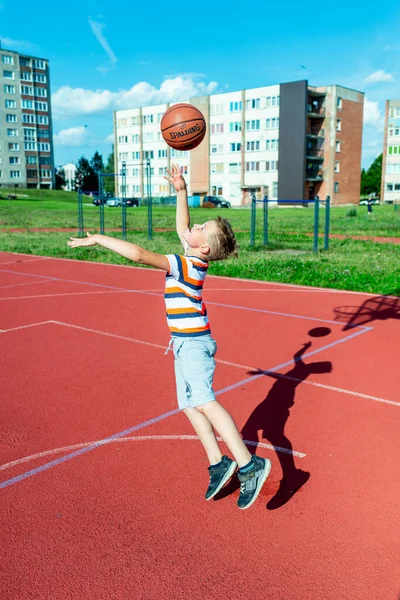 Telsiai, Litvanya 08: 12 2020 Çekici Kafkasyalı küçük basketbolcu açık havada kırmızı kortta antrenman yapıyor.