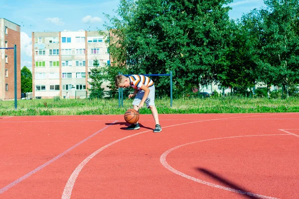 Telsiai, Litvanya 08: 12 2020 Çekici Kafkasyalı küçük basketbolcu açık havada kırmızı kortta antrenman yapıyor.