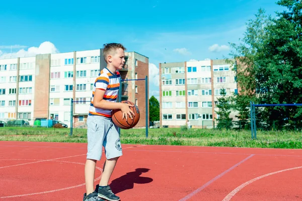 Telsiai, Litvanya 08: 12 2020 Çekici Kafkasyalı küçük basketbolcu açık havada kırmızı kortta antrenman yapıyor.