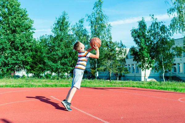 Telsiai, Litvanya 08: 12 2020 Çekici Kafkasyalı küçük basketbolcu açık havada kırmızı kortta antrenman yapıyor.