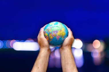 Dünyanın küresi, mavi gökyüzüne karşı insanoğlunun ellerinde bulanık şehir. İş dünyası, siyaset, ekoloji ve medya.