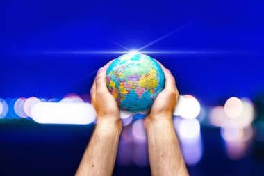 Dünyanın küresi, mavi gökyüzüne karşı insanoğlunun ellerinde bulanık şehir. İş dünyası, siyaset, ekoloji ve medya.