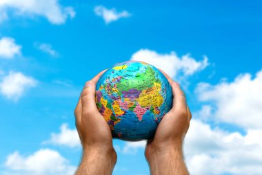 Bulanık mavi gökyüzünde ve arka plandaki duvar kağıdında küçük dünya gezegenini insan elleri tutuyor..