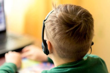 Bulanık seçici odak resmini kapat. Çocuk uzaktan öğrenerek evde öğreniyor, çocuk mikrofonlu kulaklık kullanıyor..