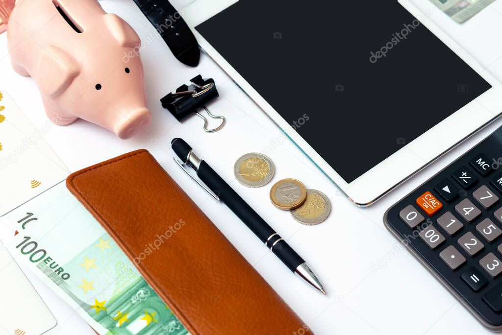 Top view close up image.Piggy bank, office supplies,pen, credit cards,calculator, clock and money on a white desk.