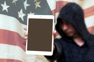 Gri kazaklı bulanık bir adam fotokopi alanı için boş ekranlı tablet bilgisayar tutuyor. Arkasında ABD bayrağı var. Seçmeli odak noktası. Görüntü ayarlı..