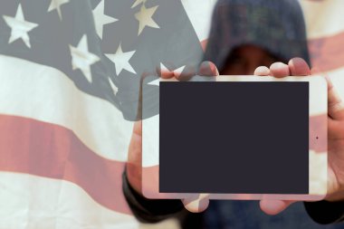 Gri kazaklı bulanık bir adam fotokopi alanı için boş ekranlı tablet bilgisayar tutuyor. Arkasında ABD bayrağı var. Seçmeli odak noktası. Görüntü ayarlı..