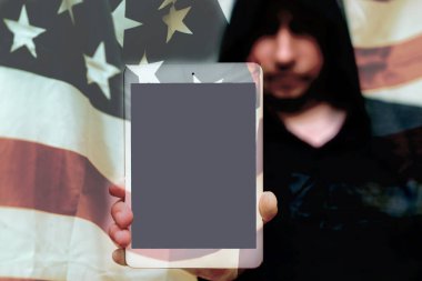 Gri kazaklı bulanık bir adam fotokopi alanı için boş ekranlı tablet bilgisayar tutuyor. Arkasında ABD bayrağı var. Seçmeli odak noktası. Görüntü ayarlı..