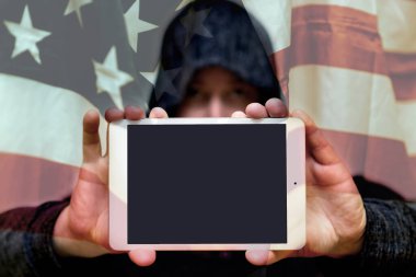 Gri kazaklı bulanık bir adam fotokopi alanı için boş ekranlı tablet bilgisayar tutuyor. Arkasında ABD bayrağı var. Seçmeli odak noktası. Görüntü ayarlı..