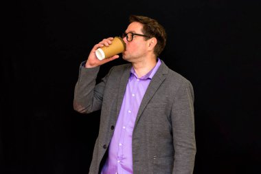 Resmi giyinmiş yakışıklı, olgun bir Amerikalı iş adamının fotoğrafı siyah arka planda duruyor, elinde içki ve içki gösterileri başparmağıyla sana kahve veriyor..