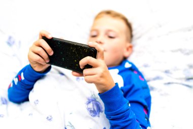 Kapat. Hasta çocuk yatakta yatarken akıllı telefona bakar ve hasta iken oyunu oynar.