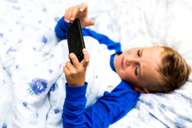Hasta çocuk yatakta yatarken akıllı telefona bakar ve hasta iken oyunu oynar.