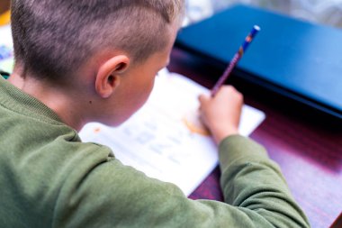 Kafkasyalı bir öğrencinin evdeki bir masada otururken ödev yapmasını yakından izle. Kitap okumak ve dersleri tamamlamak. Bir okul çocuğu ödevini yapar. Eğitim kavramı.
