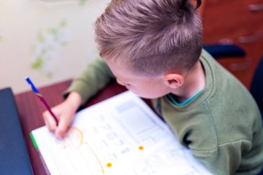 Kafkasyalı bir öğrencinin evdeki bir masada otururken ödev yapmasını yakından izleyin. Kitap okumak ve dersleri tamamlamak. Bir okul çocuğu ödevini yapar. Eğitim kavramı.