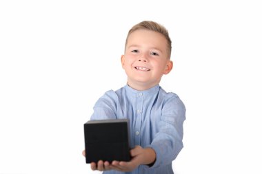 Mavi gömlekli, gülümseyen beyaz çocuk elinde siyah bir kutu tutuyor. Kutu ön tarafta. İzole edilmiş beyaz arka plan.