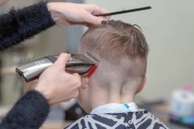 Arka plan. Mutlu çocuk berber salonunda ıslak saçlarıyla oturuyor ve saçını kesiyor..