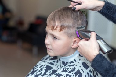 Mutlu çocuk berber salonunda ıslak saçlarıyla oturuyor ve saçını kesiyor..