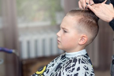 Kuaför şık bir saç stili yapar. Kadın ayakta duruyor ve sarışın çocuk için saçını kestiriyor. Yan görünüm resmi.