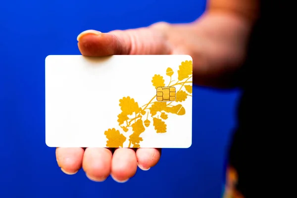 Close up woman's hand holding and showing white mockup credit card, front side view, against on defocus blur blue background. shopping concept