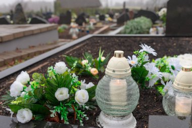 Mezarlıkta bir mum ve sahte beyaz güller. İlk kasım konsepti. Sabah.