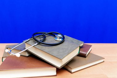 Stetoskop ve masadaki kitap yığını veya mavi modaya uygun arka plan. Tıp edebiyatı kavramı.