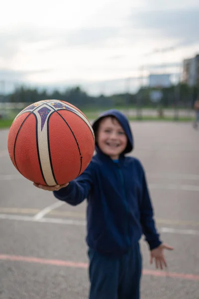 少年はボールを持って野外バスケットボールコートに立っている カメラと笑顔を見て — ストック写真
