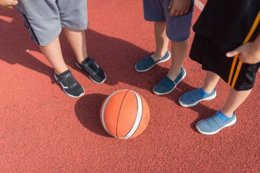 Basketbol sahasında ayakta duran bir grup genç arkadaş. Sadece bacakları görünüyor.