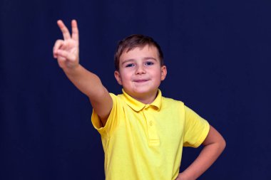 Parmakları olan çocuk mavi karanlık stüdyoda barış ya da zafer işareti gösteriyor.