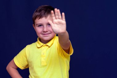 Küçük 9 'lu çocuk elini uzatıp dur işareti yapıyor. Mavi stüdyo arka planı..