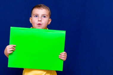 Mutlu, hoş, sakin, beyaz çocuk elinde mavi arka plan hakkında bilgi için bir poster tutuyor.